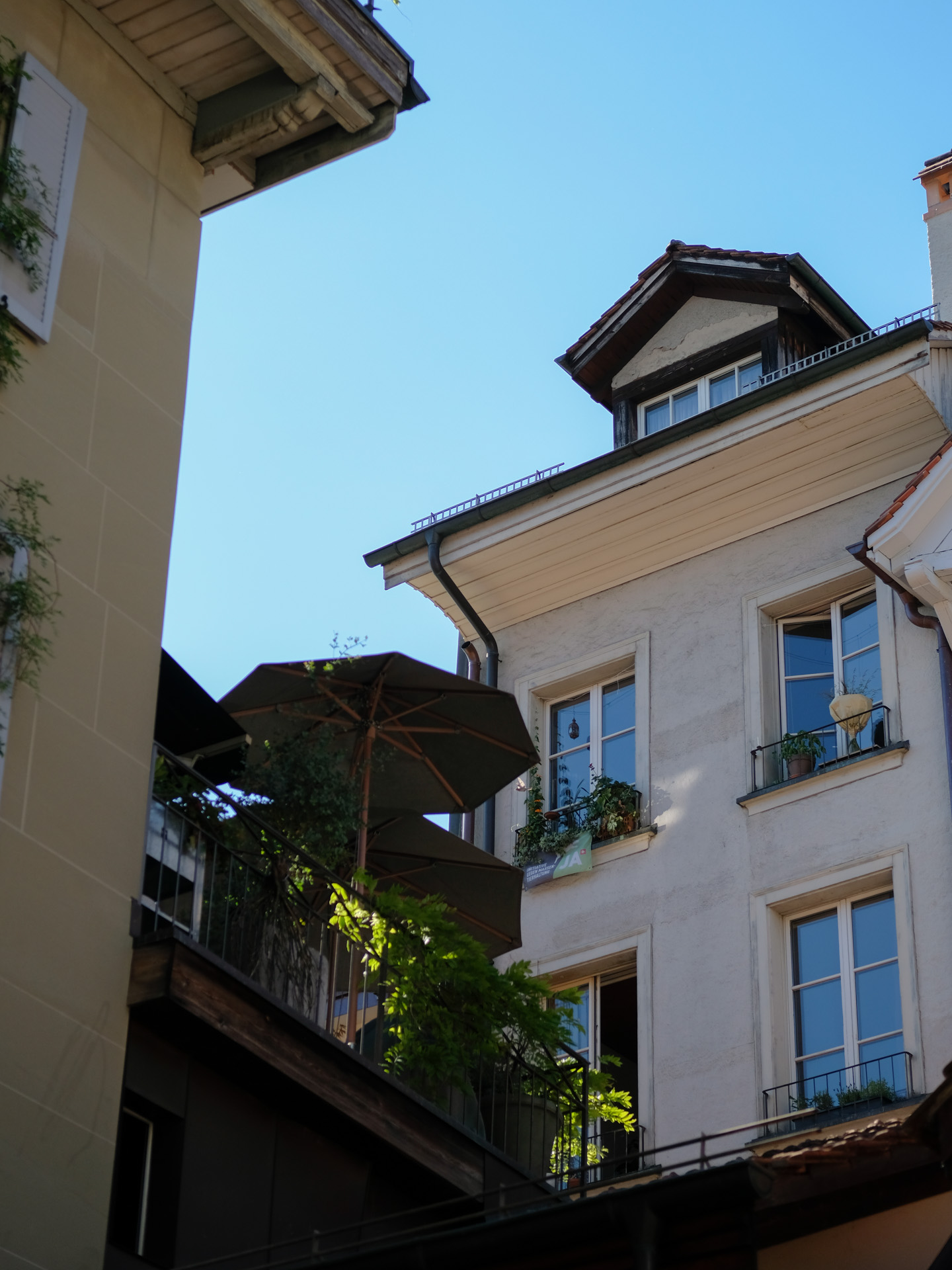 Zwei Häuser in der Altstadt mit einer Terrasse und Sonnenschirmen. Der Himmel spiegelt sich in den Fenstern.